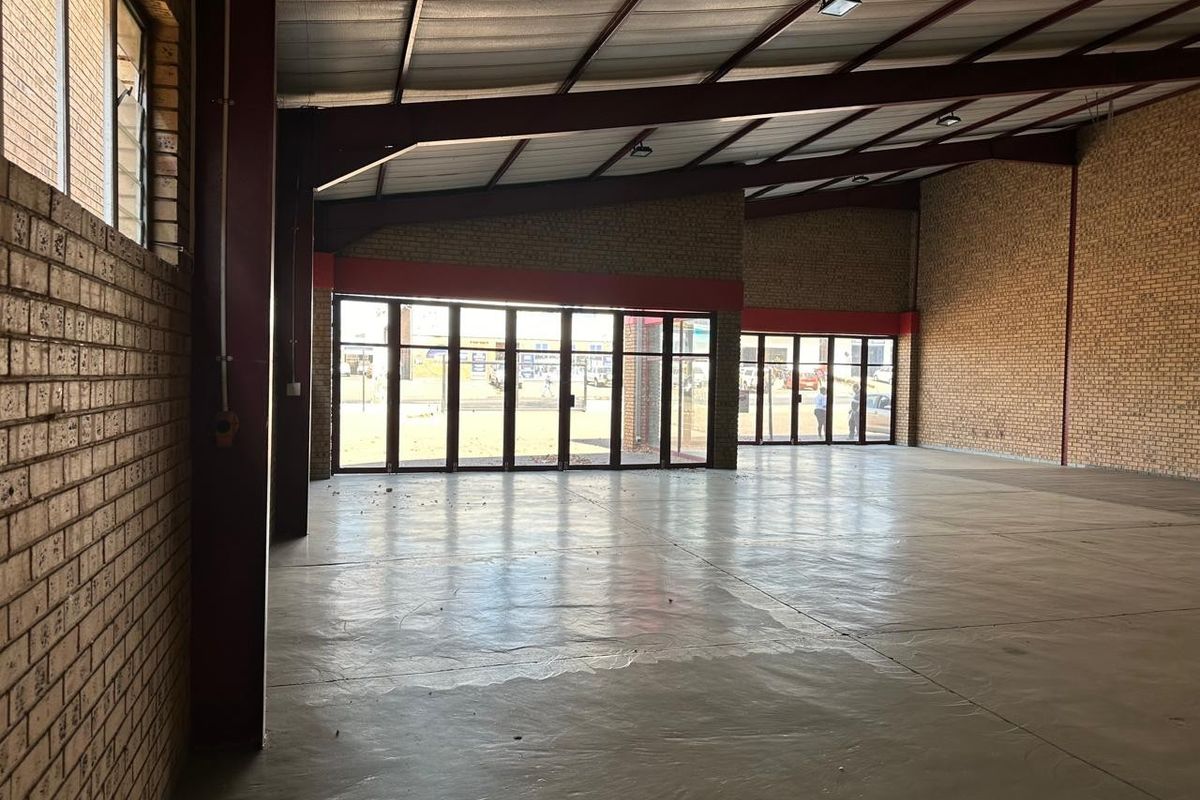 Spacious open-plan commercial warehouse area featuring exposed brick walls, high-pitched steel roof structure, and large glass folding doors providing ample natural light.