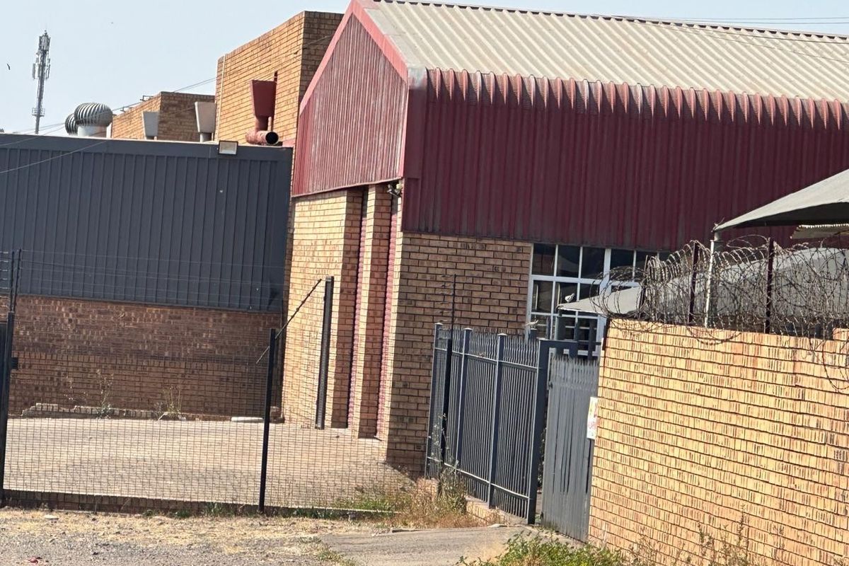 Exterior view of a commercial industrial building featuring brick facade, corrugated metal roofing, and secure perimeter fencing.