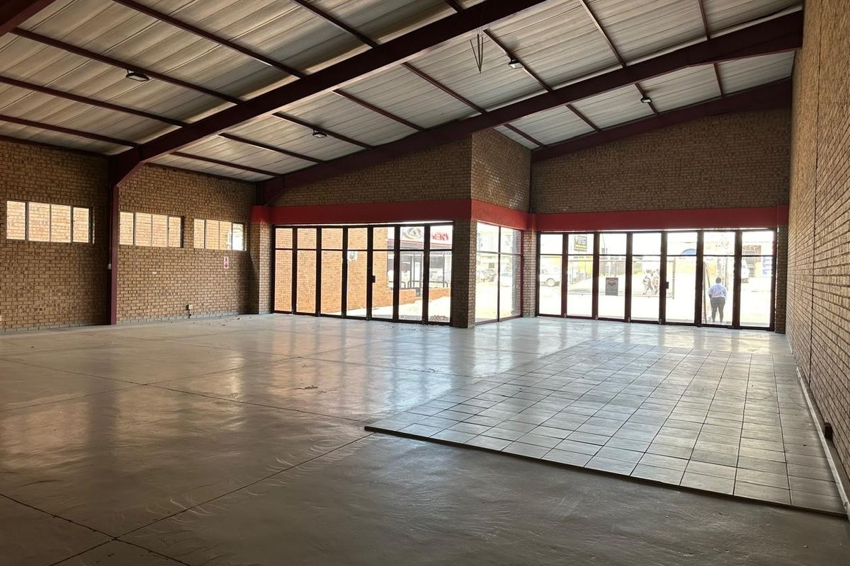 Spacious open-plan commercial unit featuring exposed brick walls, high-pitched steel truss ceiling, and large glass folding doors providing ample natural light.