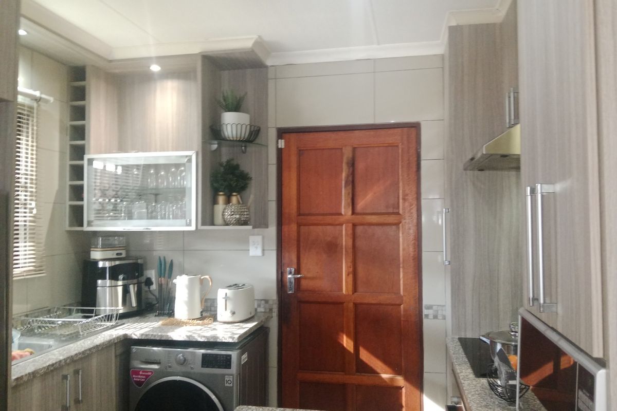A functional kitchen featuring modern wood-grain cabinetry, granite countertops, a built-in extractor fan, and integrated space for a washing machine.