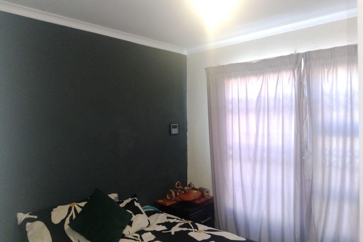 A bedroom featuring a dark accent wall, coved ceiling cornices, and window treatments.
