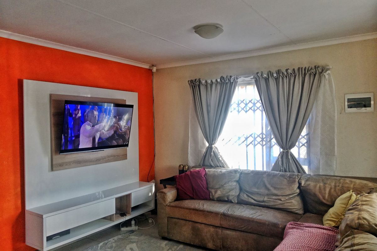 A living room featuring a built-in media console and wall-mounted television unit, complemented by a window with security gate and curtain fixtures.