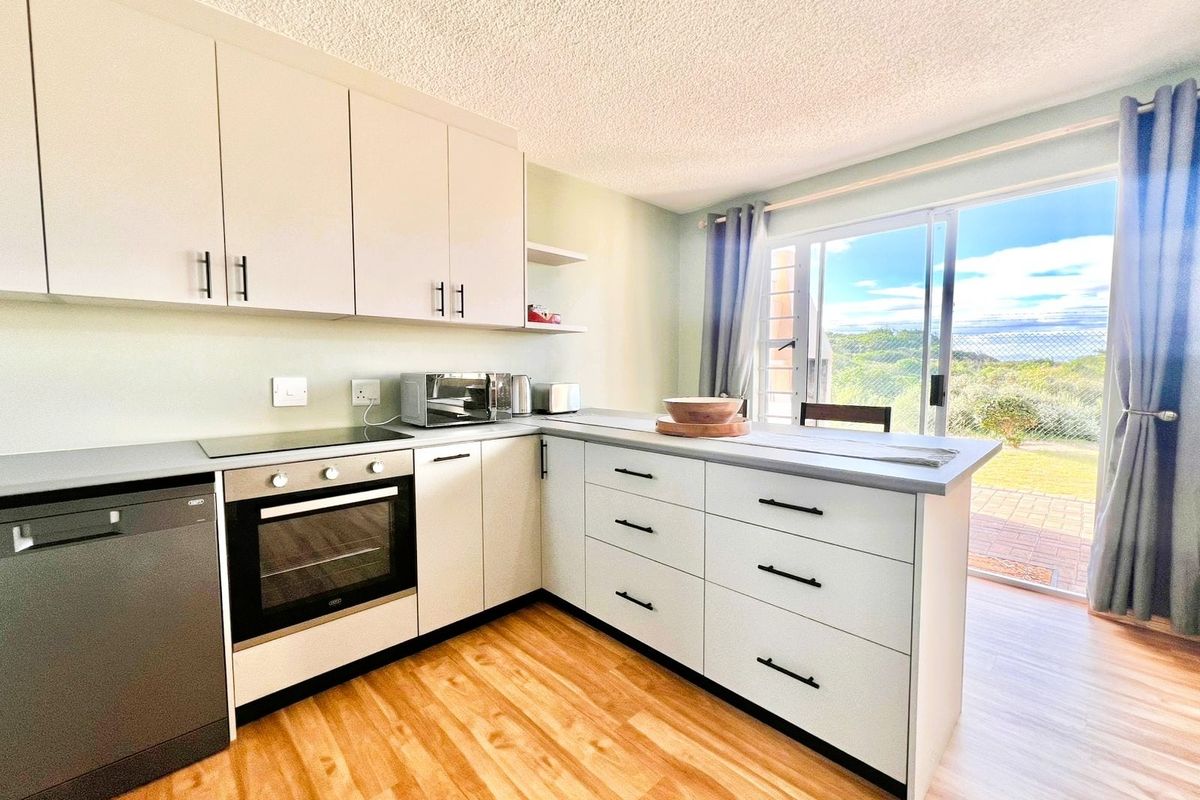 Modern kitchen featuring light-toned cabinetry, built-in oven, hob, and integrated dishwasher, with direct access to an outdoor patio area.