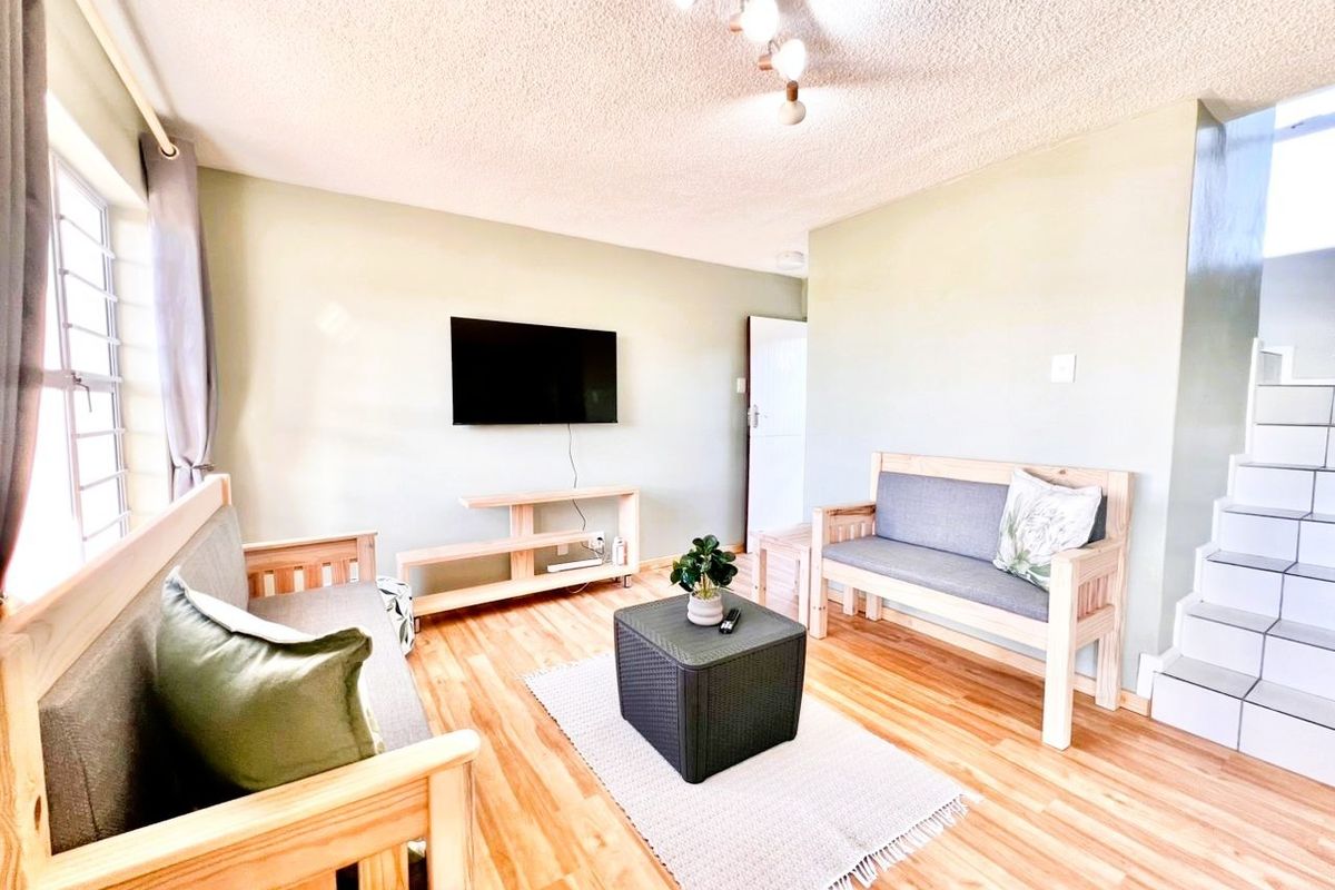 A living room featuring light wood-look flooring, a textured ceiling, and a staircase leading to the upper level.