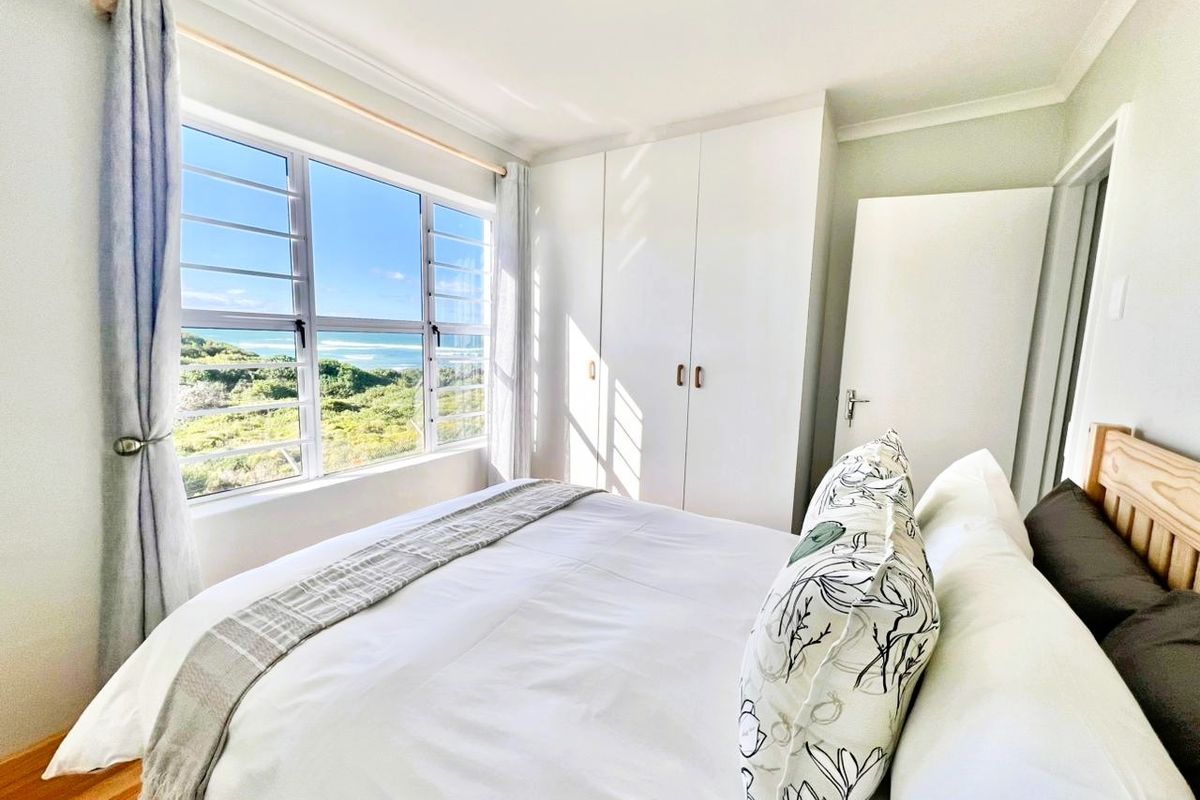 A bright bedroom featuring built-in cupboards and a large window offering scenic coastal views.