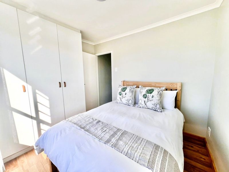 A bright bedroom featuring built-in wardrobes with white cabinetry and warm-toned wood-look flooring.