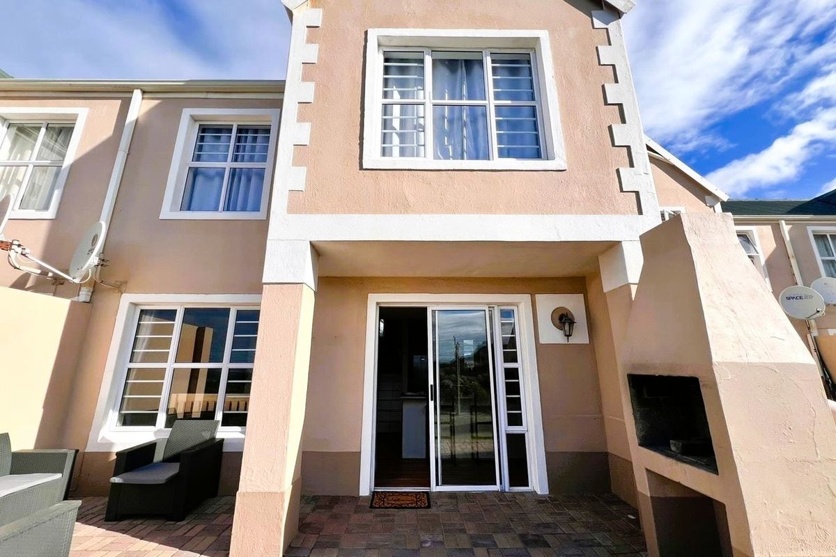 Rear exterior view of the apartment featuring a paved patio area, built-in braai, and sliding glass door access to the interior living space.