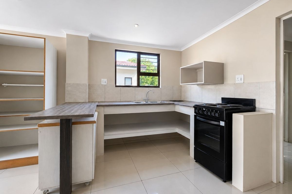A functional kitchen featuring tiled flooring, a built-in sink, tiled splashbacks, and a freestanding stove, offering a clean and practical workspace.