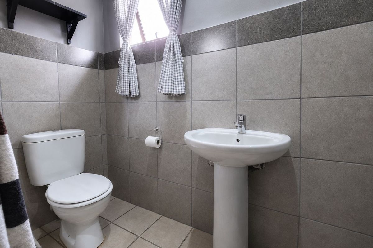 A functional bathroom featuring a pedestal basin, a standard toilet, and neutral wall tiling.