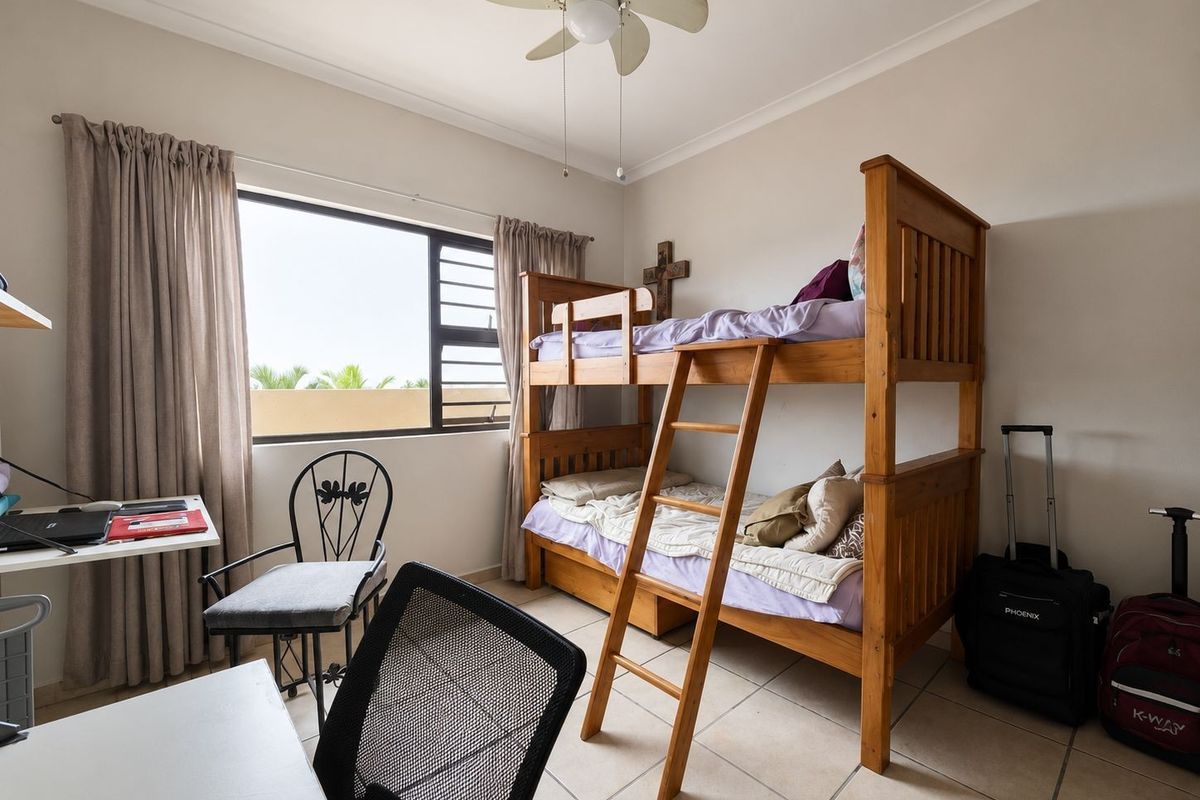 A functional bedroom featuring tiled flooring, a ceiling fan, and a large window providing natural light.