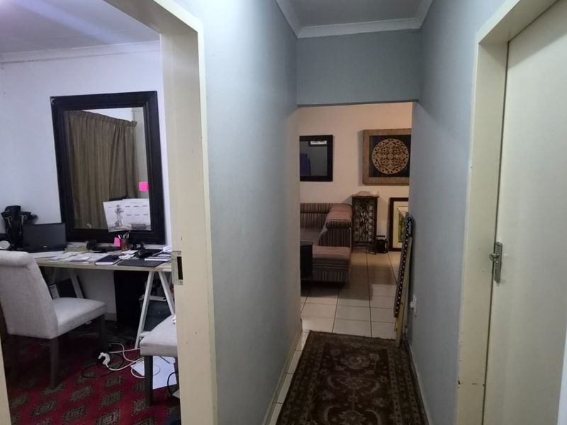 A functional hallway connecting multiple rooms, featuring neutral wall finishes and tiled flooring, providing access to the living area and adjacent office space.