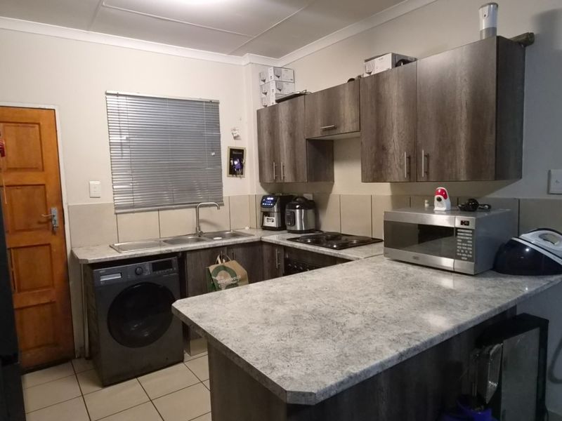 A functional kitchen featuring dark wood-look cabinetry, stone-effect countertops, integrated hob, and tiled flooring with a practical layout.