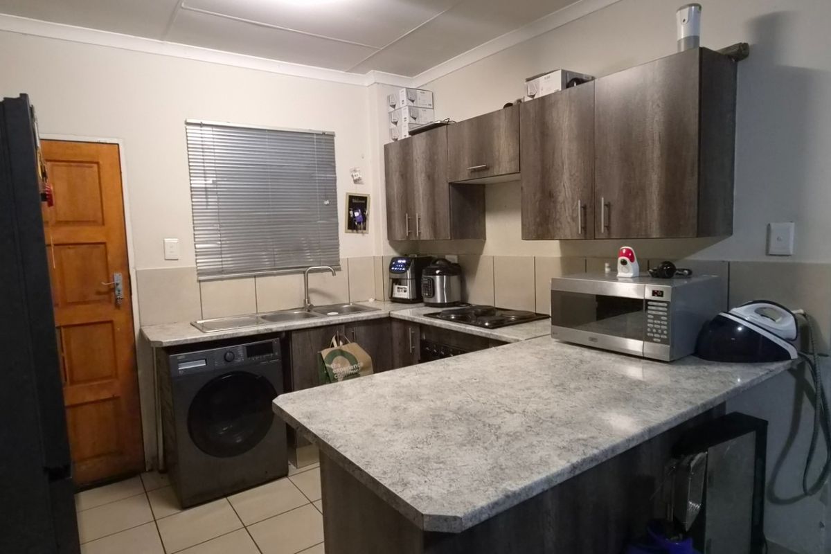 A functional kitchen featuring dark wood-look cabinetry, stone-effect countertops, integrated hob, and tiled flooring with a practical layout.