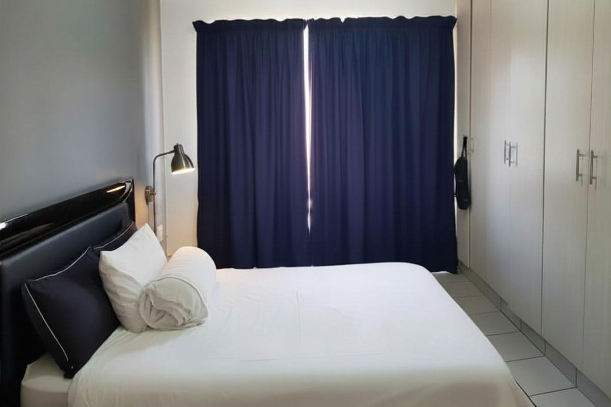 A well-maintained bedroom featuring built-in floor-to-ceiling wardrobes, tiled flooring, and a neutral color palette with a feature wall.