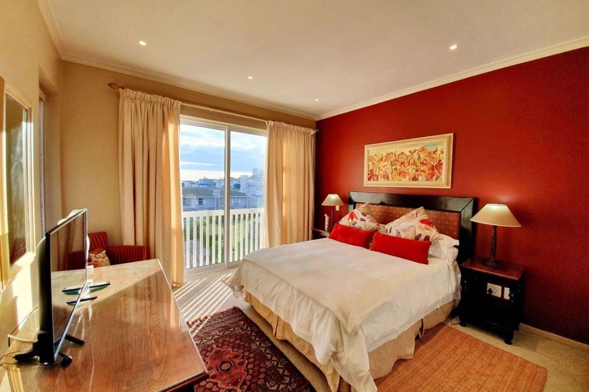 A well-lit bedroom featuring a sliding glass door leading to a private balcony, recessed ceiling lighting, and a prominent accent wall.