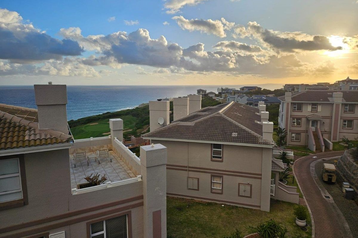 Elevated aerial view of the apartment complex featuring tiled roofing, chimneys, and a scenic coastal landscape with ocean views.