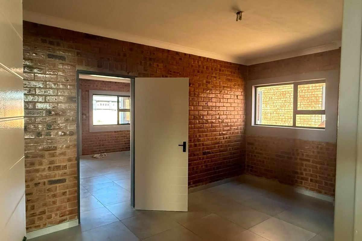 An interior view of an industrial-style room featuring exposed brick walls, tiled flooring, and a doorway leading to an adjacent space.
