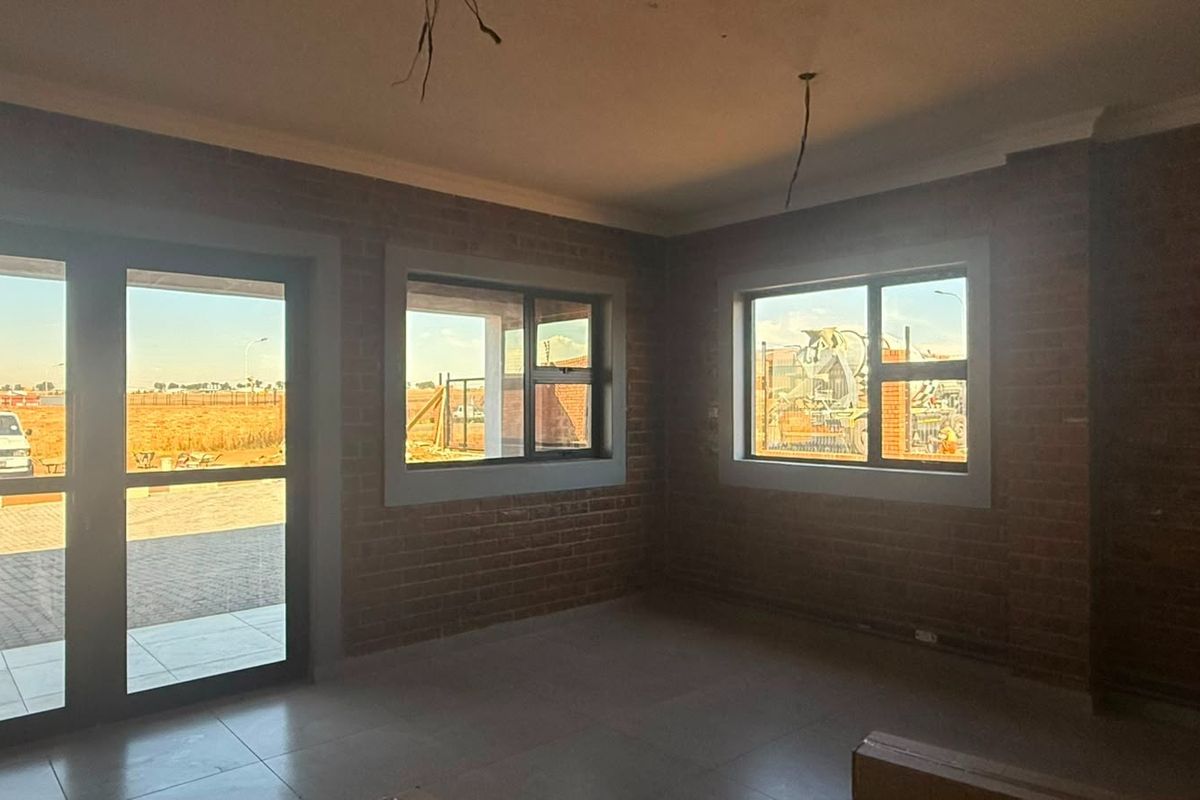 An unfinished interior space featuring exposed brick walls, tiled flooring, and large windows with views of the surrounding industrial site.
