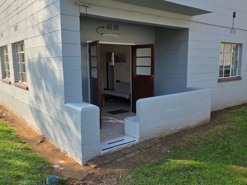 A ground-level apartment entrance featuring a small covered patio area with concrete walls and double wooden doors leading into the interior.