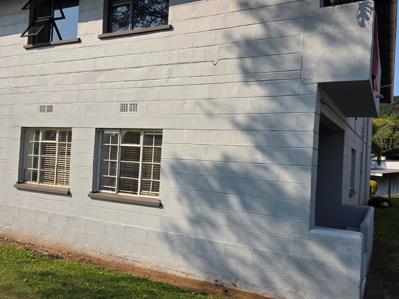 Exterior view of the apartment building featuring painted masonry walls, metal-framed windows with security bars, and a covered entrance area.