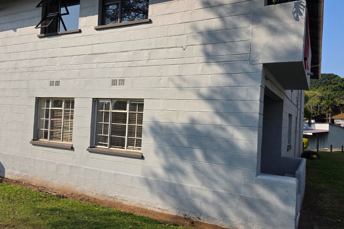Exterior view of the apartment building featuring painted masonry walls, metal-framed windows with security bars, and a covered entrance area.