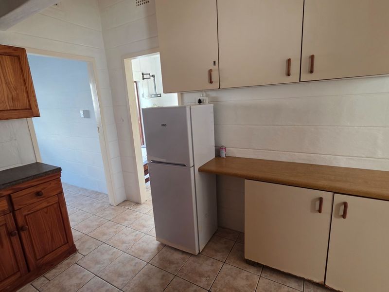 A functional kitchen area featuring a mix of wooden and laminate cabinetry, tiled flooring, and a laminate countertop.