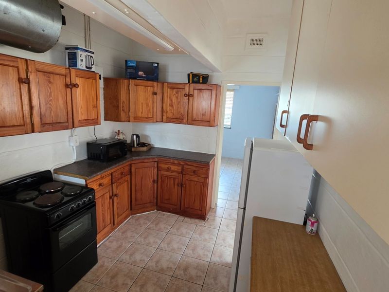 A functional kitchen featuring wooden cabinetry, dark laminate countertops, tiled flooring, and a freestanding stove, with an adjacent view into another room.