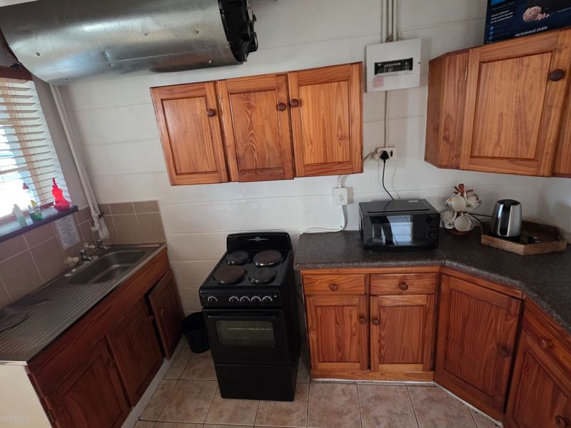A functional kitchen featuring wooden cabinetry, a freestanding stove, a stainless steel sink, and tiled flooring.