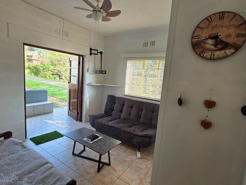 A living room featuring tiled flooring, a ceiling fan, and direct access to an outdoor patio area through a wooden door.
