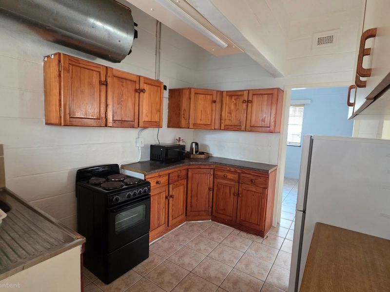 A functional kitchen featuring timber cabinetry, tiled flooring, and a freestanding electric stove, offering a practical layout for daily meal preparation.