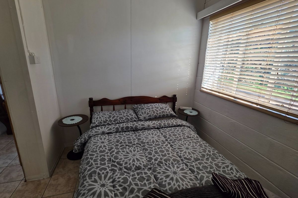 A compact bedroom featuring tiled flooring and horizontal window blinds, providing a functional and simple sleeping space.