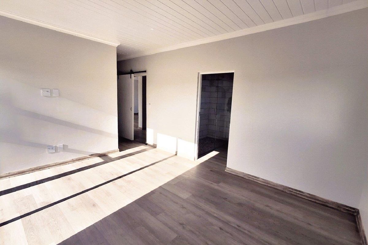 A bright, empty bedroom featuring modern wood-look laminate flooring, a white tongue-and-groove ceiling, and direct access to an en-suite bathroom.