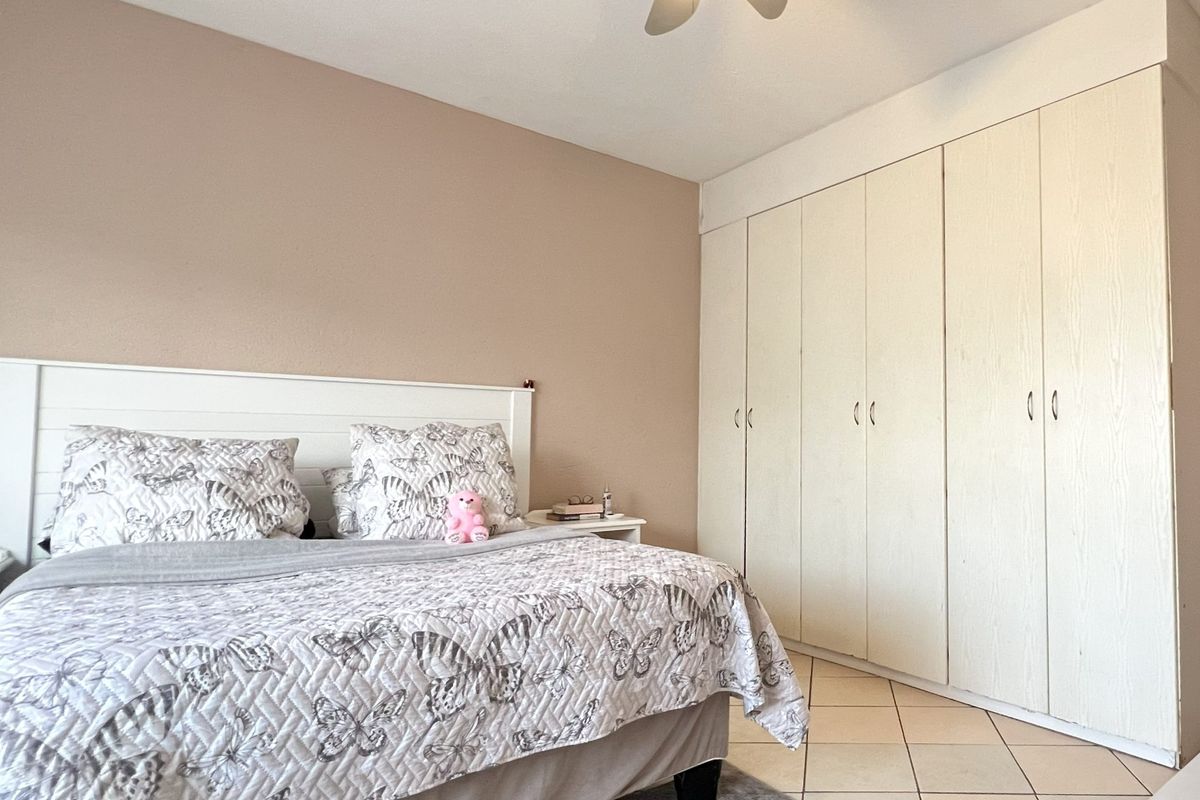 A bedroom featuring built-in floor-to-ceiling wardrobes, tiled flooring, and a ceiling fan.