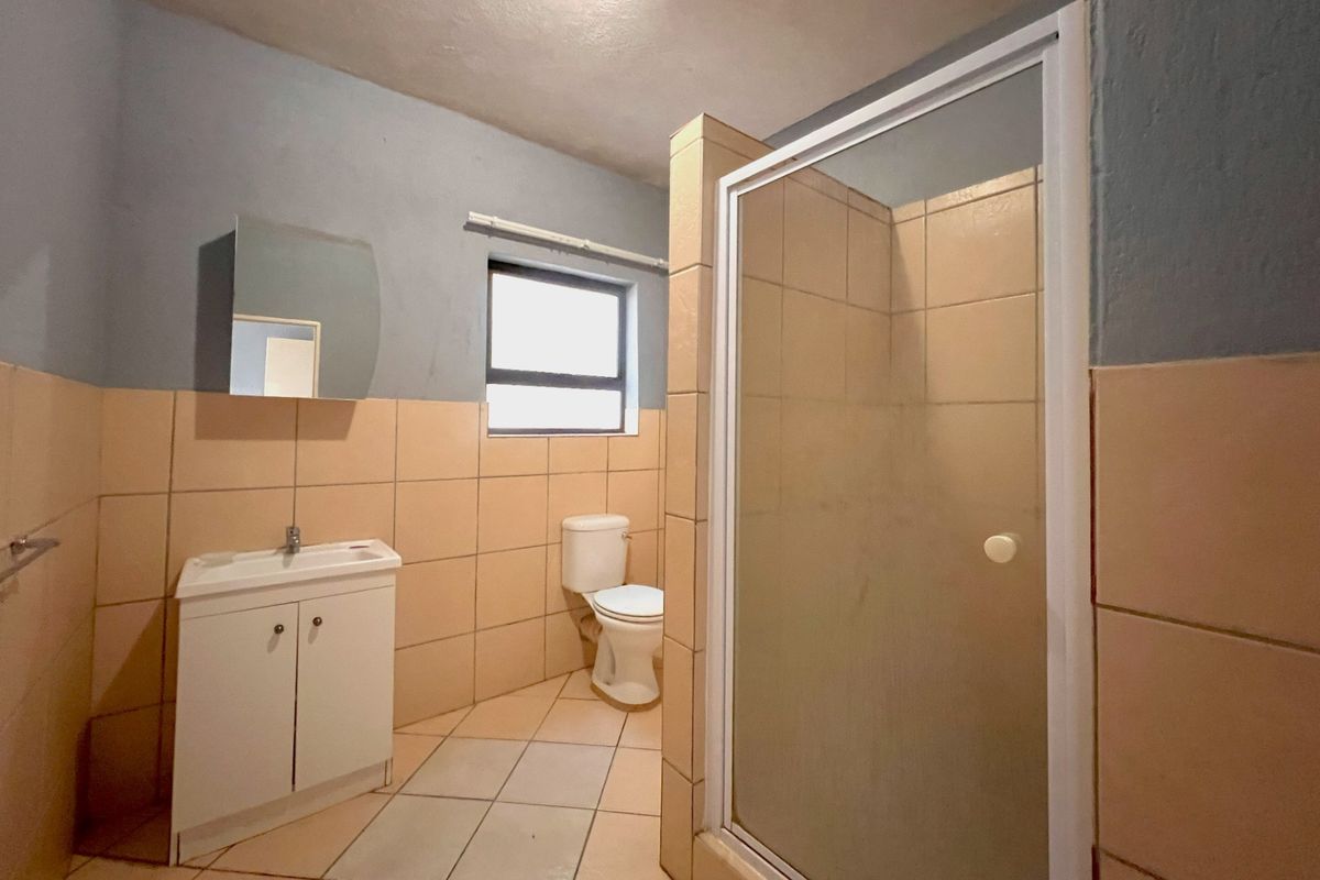 A functional bathroom featuring a tiled shower enclosure, a vanity basin with mirror, and a standard toilet, finished with neutral wall and floor tiles.