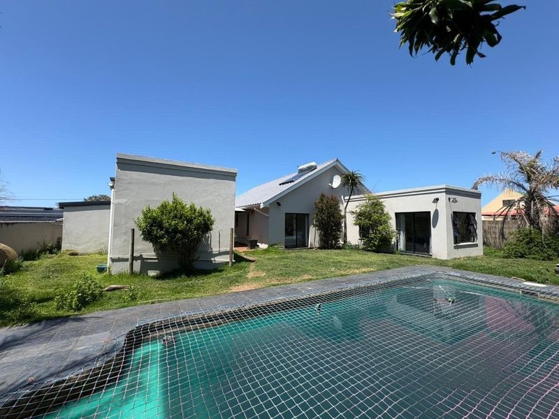 Rear view of the property featuring a swimming pool with a safety net, landscaped garden area, and direct access via sliding glass doors.