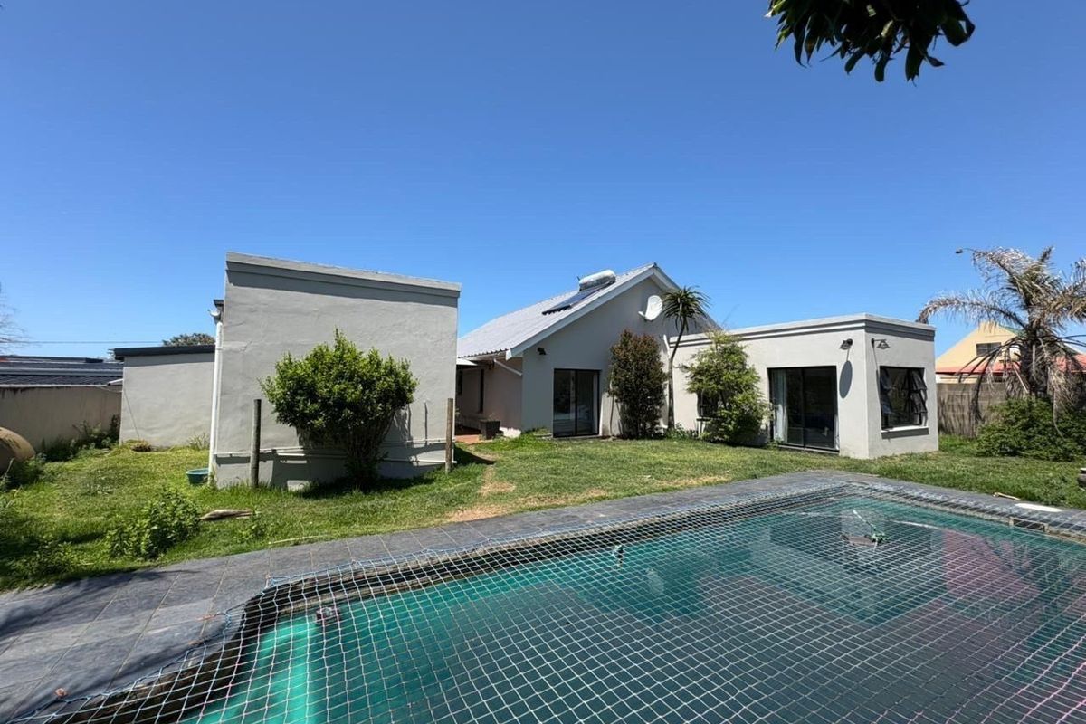 Rear view of the property featuring a swimming pool with a safety net, landscaped garden area, and direct access via sliding glass doors.