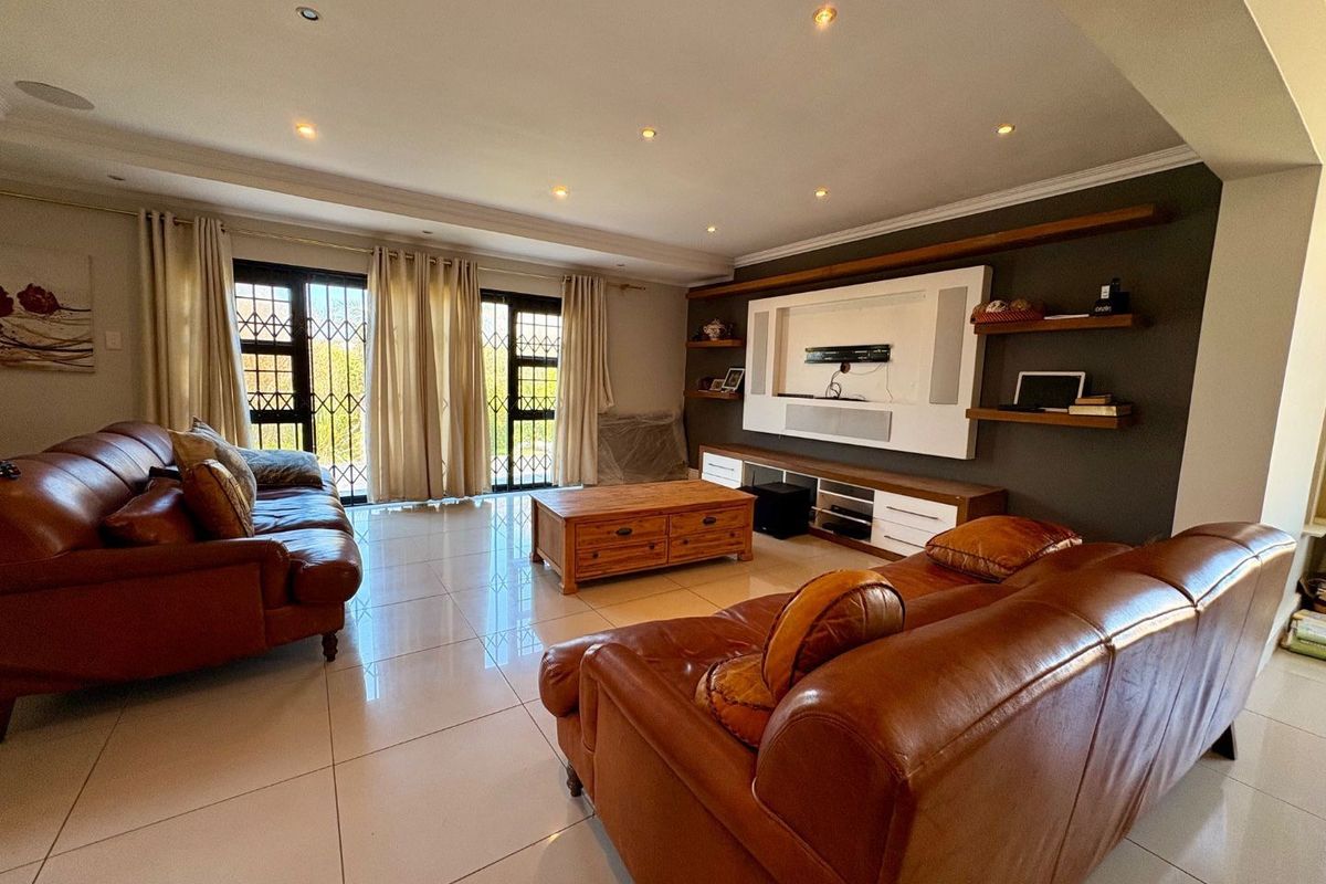 Spacious living room featuring tiled flooring, recessed downlights, and a custom built-in media unit with integrated shelving.