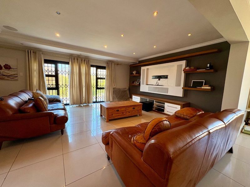 Spacious living room featuring tiled flooring, recessed downlights, and a custom built-in media unit with integrated shelving.