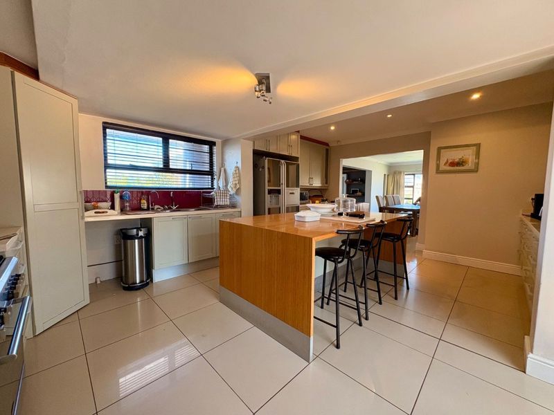 Open-plan kitchen featuring a central wooden island, tiled flooring, and ample built-in cabinetry, seamlessly flowing into the adjacent dining area.