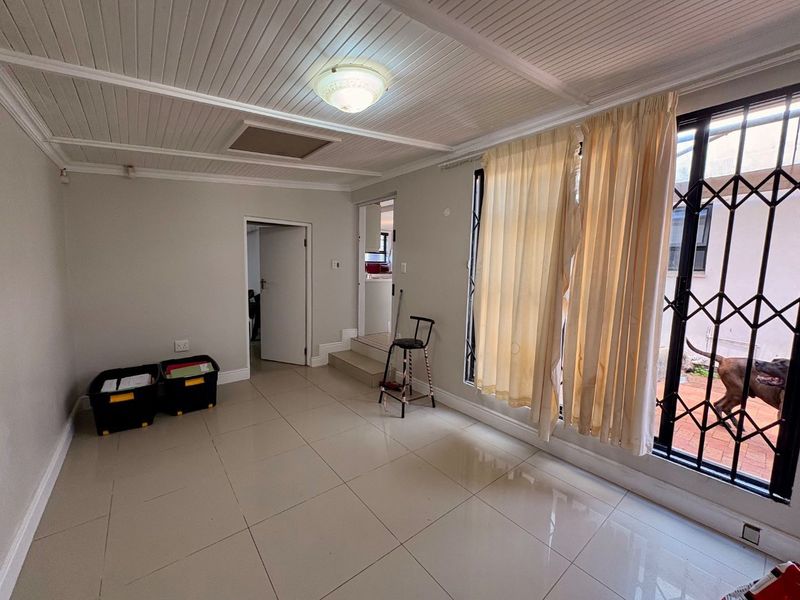 An empty living area featuring tiled flooring, a tongue and groove ceiling, and a sliding door with a security gate leading to the exterior.