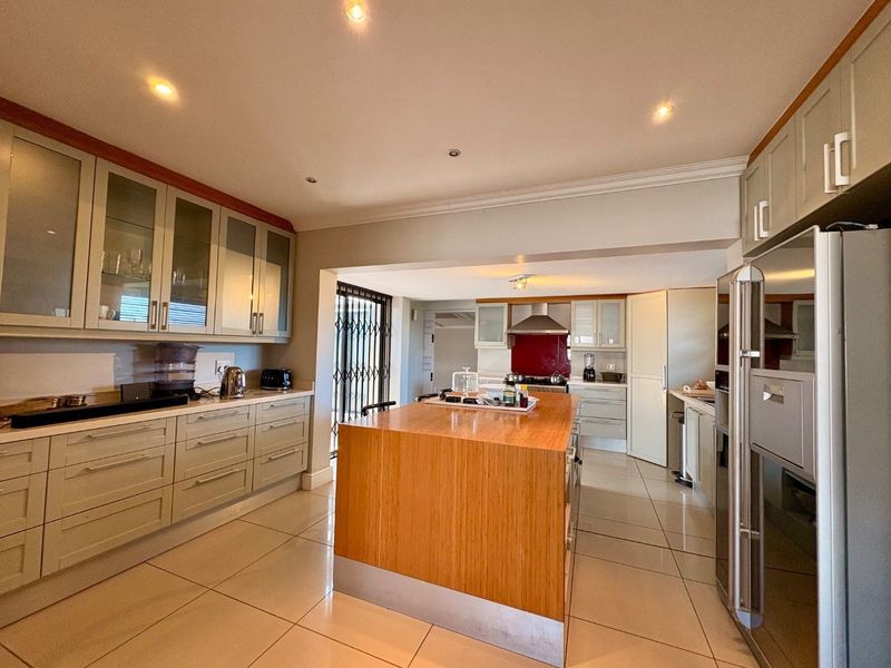 Spacious modern kitchen featuring a large central island, extensive built-in cabinetry, tiled flooring, and integrated appliances with recessed lighting throughout.
