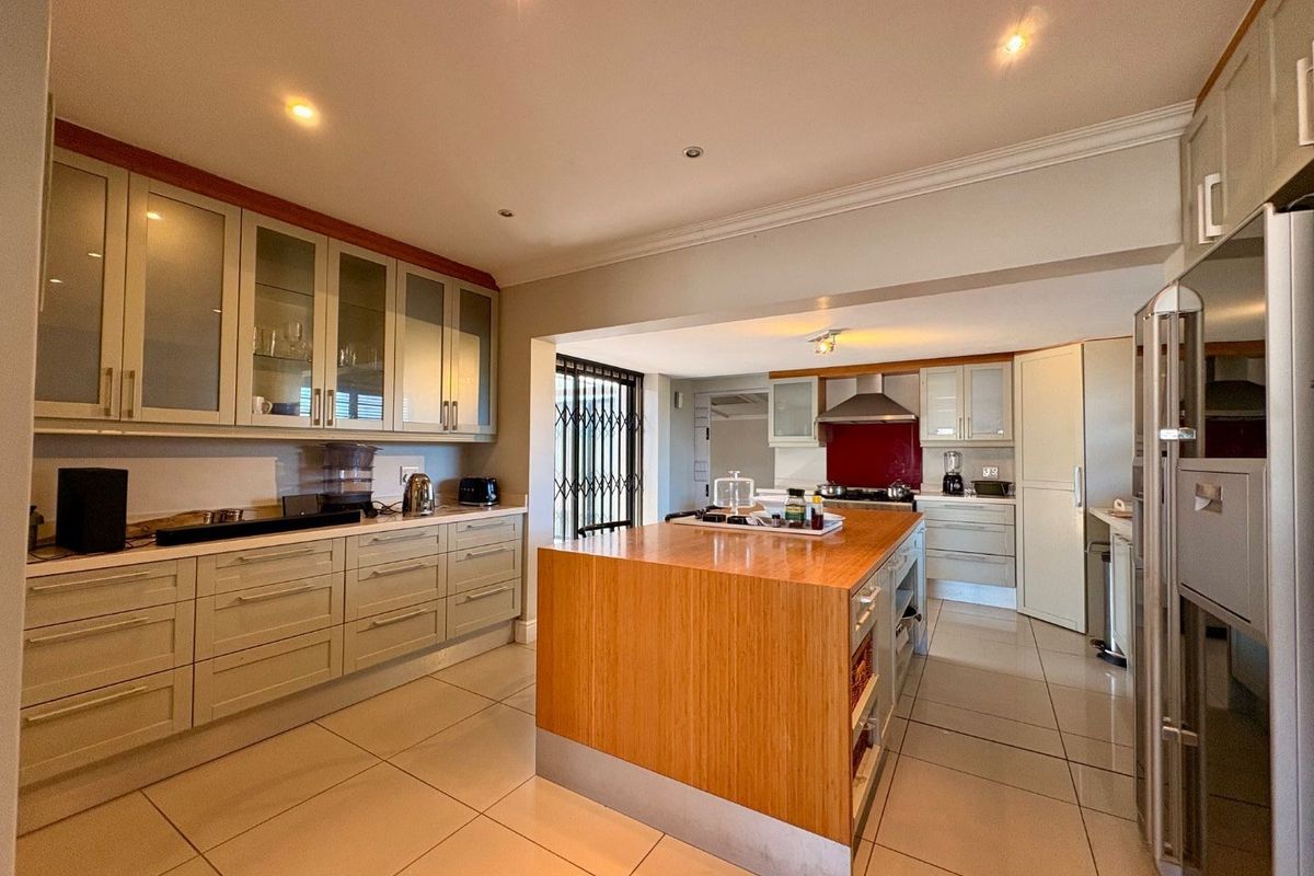 Spacious kitchen featuring a large central island, extensive built-in cabinetry, modern tiled flooring, and integrated cooking appliances.