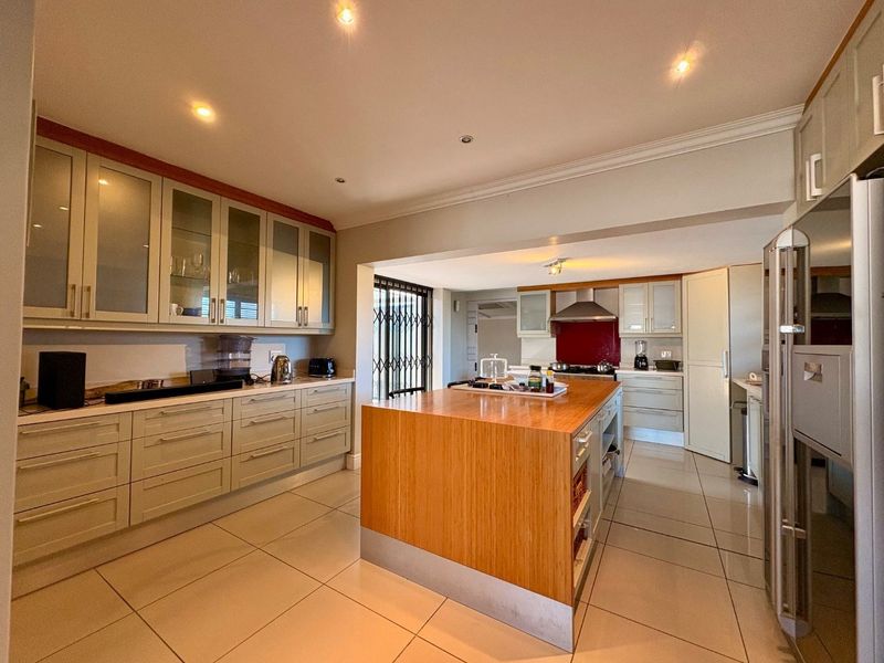 Spacious kitchen featuring a large central island, extensive built-in cabinetry, modern tiled flooring, and integrated cooking appliances.