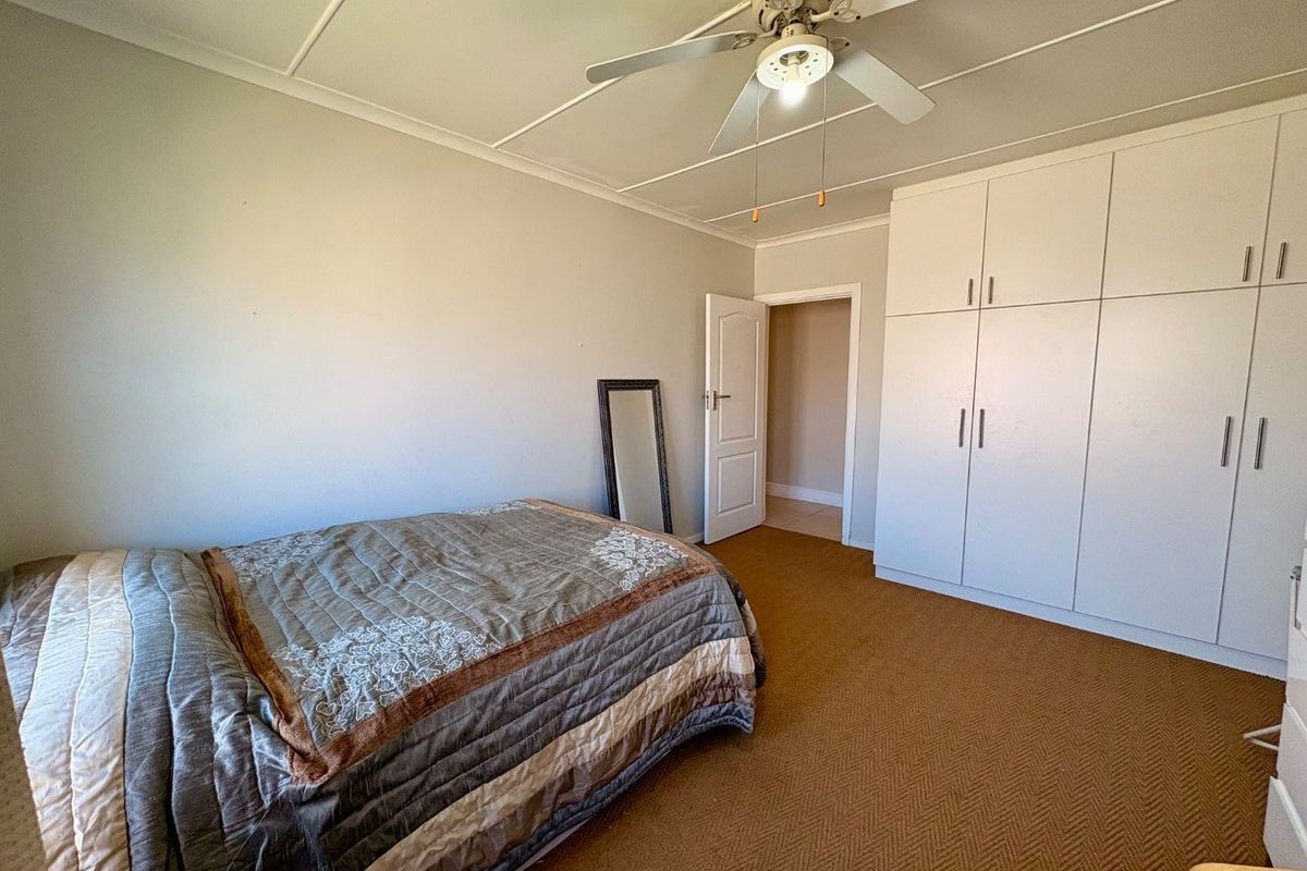 A bedroom featuring built-in cupboards, a ceiling fan, and carpeted flooring, offering a functional space with potential for cosmetic updates.