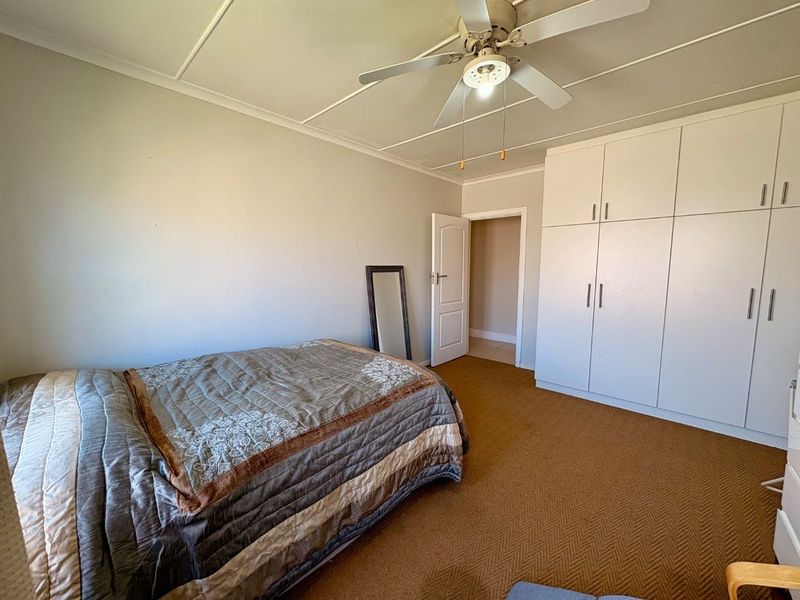 A bedroom featuring built-in cupboards, a ceiling fan, and carpeted flooring, offering a functional space with potential for cosmetic updates.
