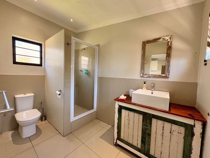A functional bathroom featuring a shower enclosure, a modern vessel sink on a rustic vanity cabinet, and neutral tiled finishes.