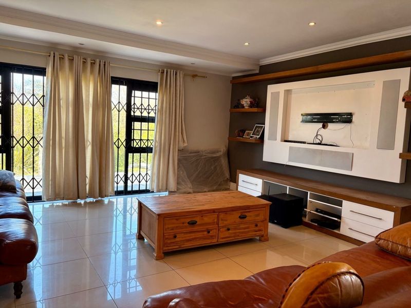 Spacious living room featuring large sliding glass doors with security gates, tiled flooring, and a custom built-in media wall unit.