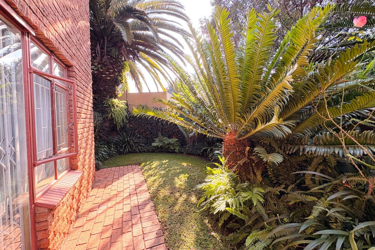 A private rear garden area featuring established cycads, lush greenery, and a brick-paved pathway adjacent to the home's brick exterior wall.