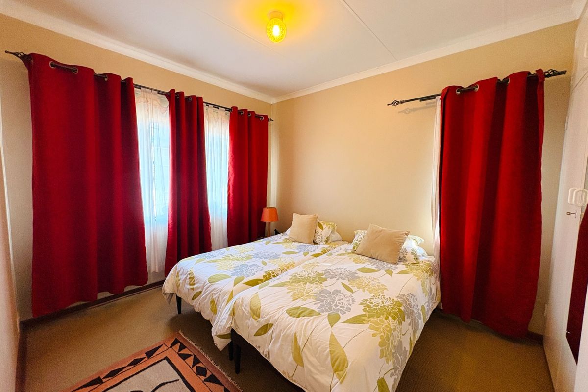 A standard bedroom featuring neutral wall paint, carpeted flooring, and dual window treatments with curtain rods.