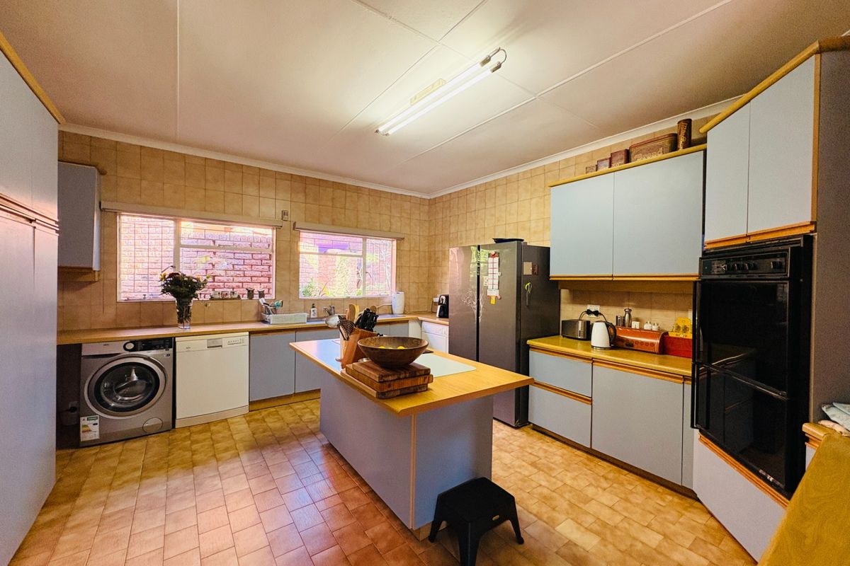 Spacious kitchen featuring built-in cabinetry, laminate countertops, tiled splashbacks, and a central island, offering a functional layout with potential for modern updates.